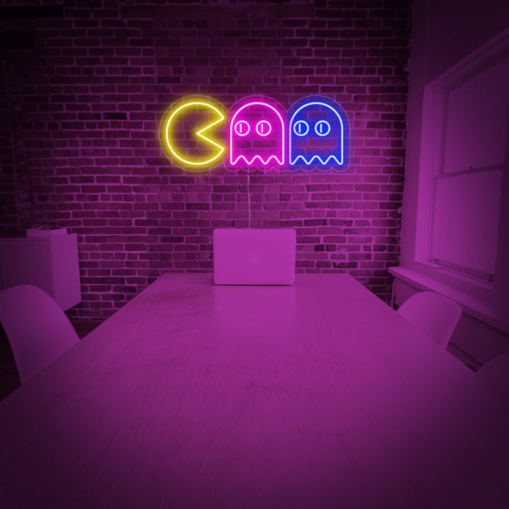 Geel Pac-Man neon LED-bord met twee kleurrijke spoken, retro decoratie op bakstenen muur.