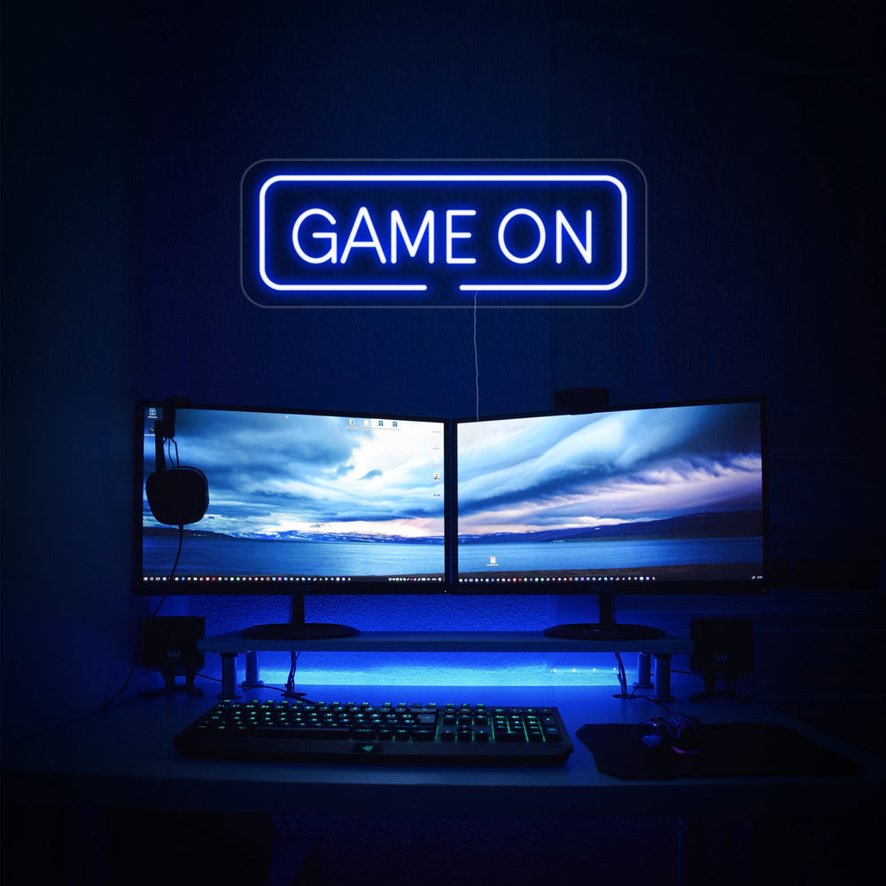 Blauw neon LED “GAME ON” boven dual-monitor setup, decoratie voor gaming room.
